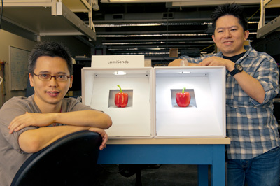 LumiSands cofounders Chang-Ching Tu, left, and Ji Hoo with with a demo showing the warmer, softer hue of the LED bulb (left side) after a film embedded with their red-emitting silicon nanoparticles is placed underneath. The box on the right is an identical, standard LED bulb.