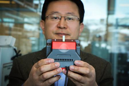 University of Utah materials science and engineering professor Ling Zang holds up a prototype handheld detector his company is producing that can sense explosive materials and toxic gases. His research team developed a new material for the detector that can sense alkane fuel, a key ingredient in such combustibles as gasoline, airplane fuel and homemade bombs. Photo credit: Dan Hixson/University of Utah College of Engineering